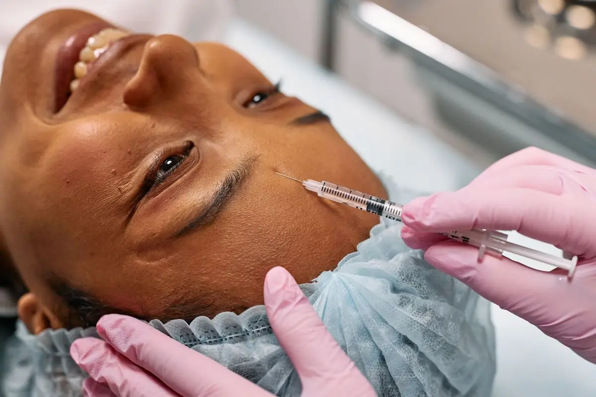 Provider in pink gloves injecting a client's forehead with a neuromodulator